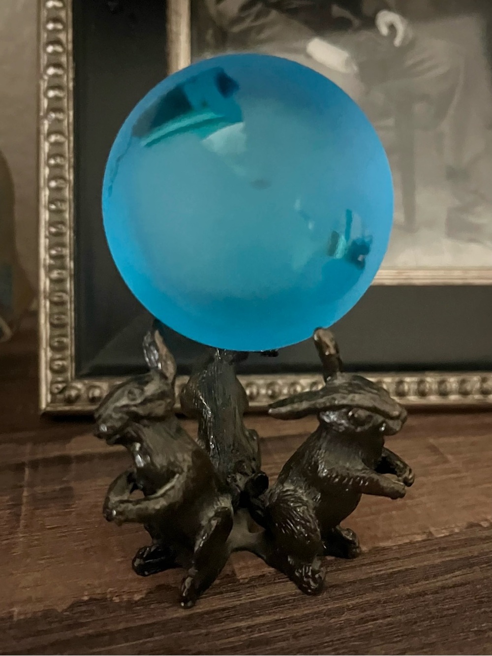 Vibrant blue glass sphere resting on a metallic hare or rabbit trio stand